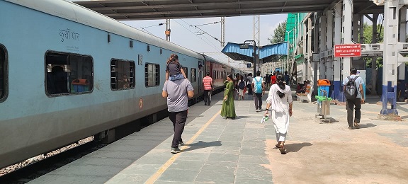 रेलवे स्टेशन पर खड़ी रेलगाड़ी और बाहर टहलते यात्री।